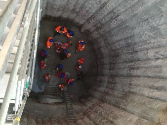 Blick in die 10 m Tiefe kreisförmige Baugrube; unten Arbeiter