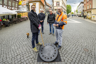 zwei Männer heben einen Gullideckel mit Haken an, zwei weitere Männer stehen dahinter