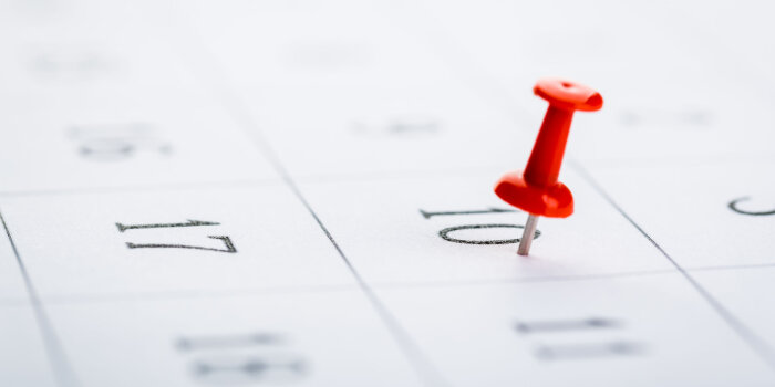 Eine rote Pinnadel steckt in einem Tag eines Kalenders.